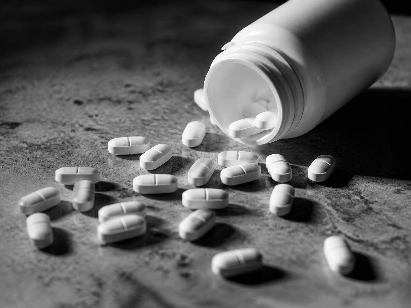 Tablets spilled from an overturned pill bottle in stark black and white